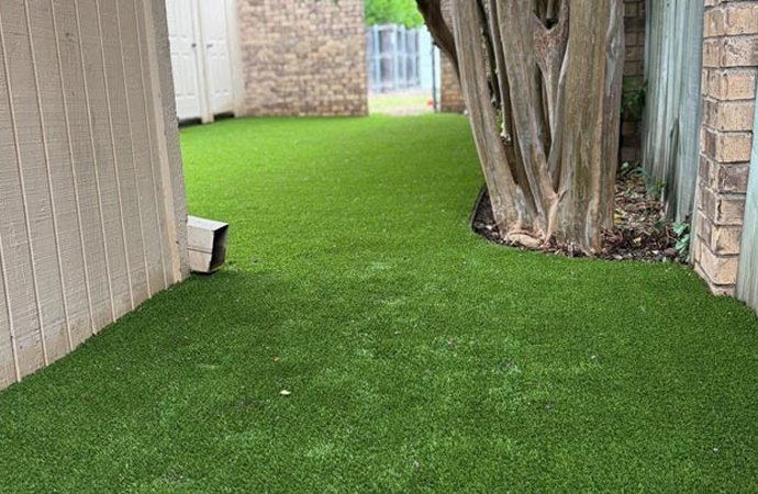 Artificial grass installed in a narrow side yard with a tree and fenced walls