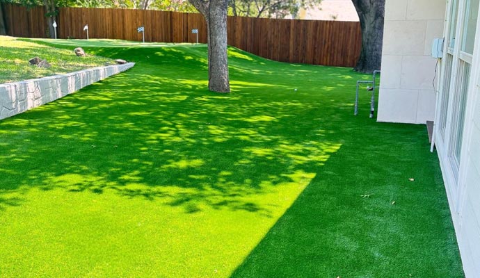 Artificial grass installed in a residential backyard with trees and wooden fence