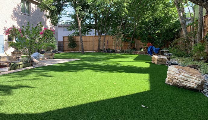 Artificial grass lawn in a backyard with landscaping rocks and trees