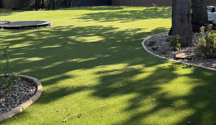 Well-maintained artificial turf backyard with landscaped borders and trees