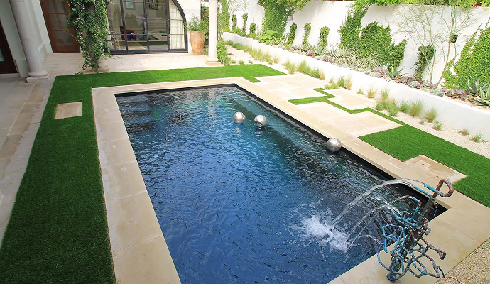 Modern backyard featuring a pool surrounded by artificial turf and a decorative water feature