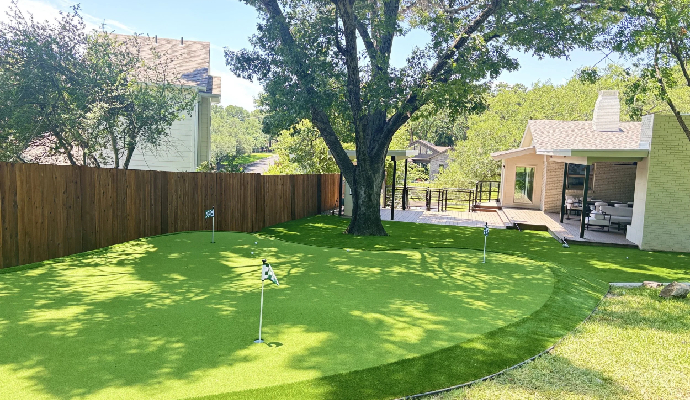 Custom backyard putting green with artificial turf surrounded by trees and a wooden fence
