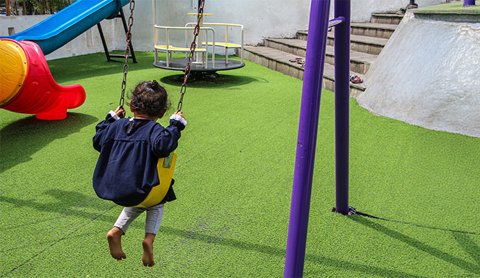Child on swing in playground with artificial grass