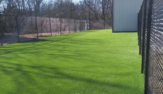Artificial grass installed in a fenced outdoor area beside a building