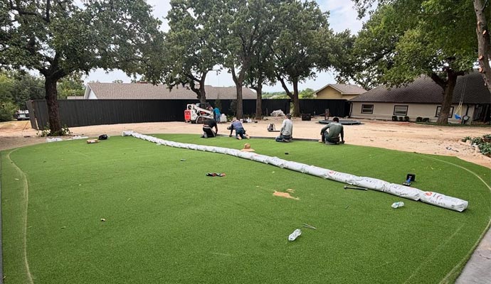 An expert team installing artificial grass on a large yard during landscaping project