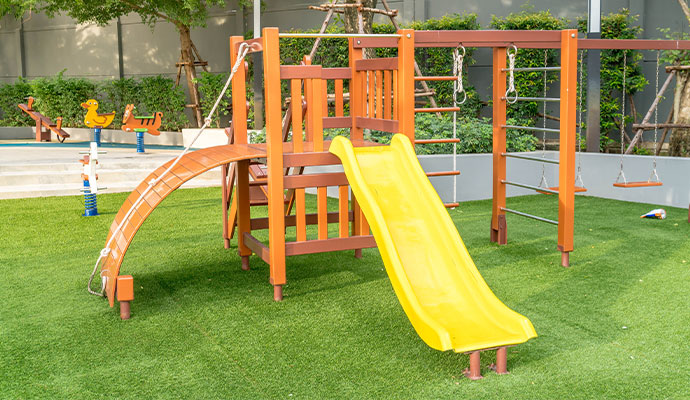 Outdoor playground with wooden playset and yellow slide installed on artificial grass