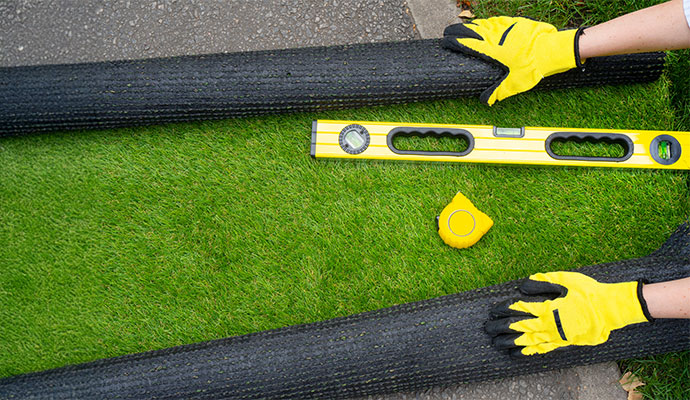 Artificial grass installation with black turf rolls and yellow leveling tool