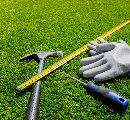 Hammer, screwdriver, measuring tape and gloves placed on artificial grass during restoration