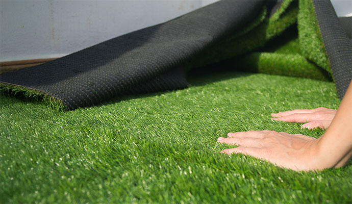 Expert adjusting synthetic turf during artificial grass installation with black backing layer visible
